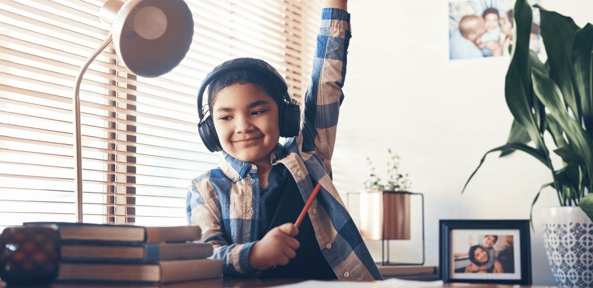 A boy wearing headphones sits at a desk, focused on his laptop, immersed in his work or entertainment.