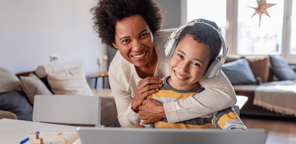 A woman and a child sit together on a couch, engaged with a laptop in a cozy living room setting.